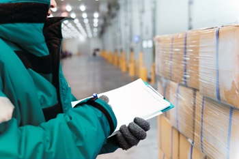 Worker with Clipboard Looking at Pallet of Boxes